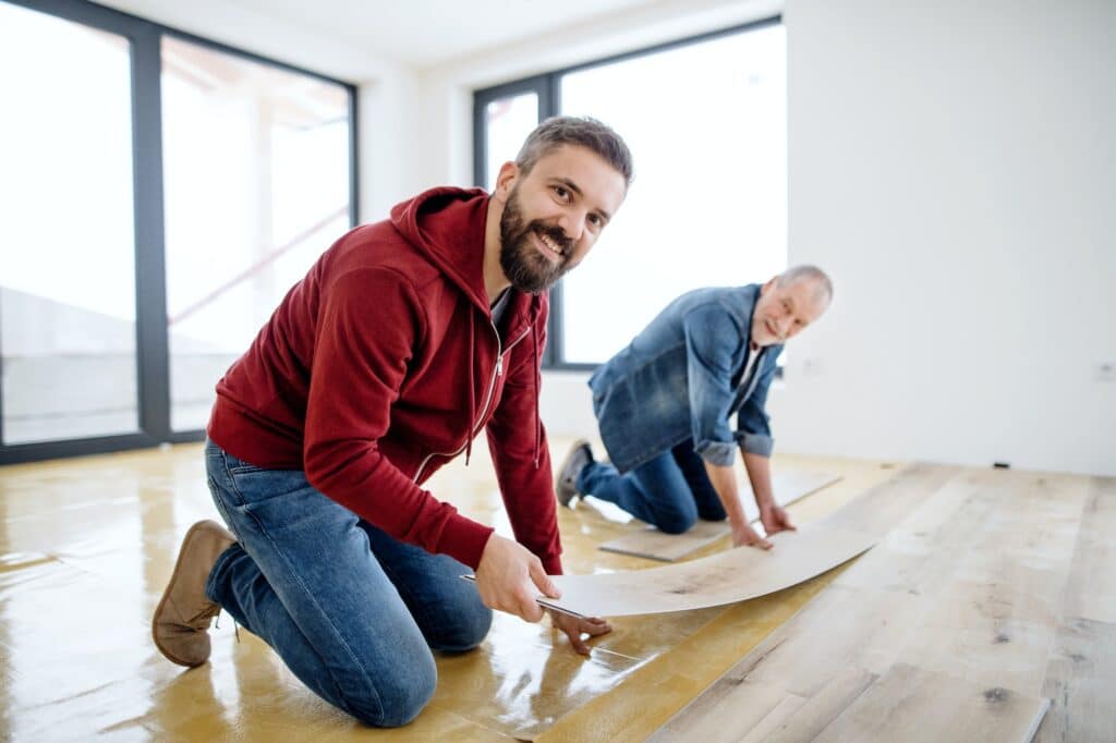 A Mature Man With His Senior Father Laying Vinyl Flooring A New Home Concept