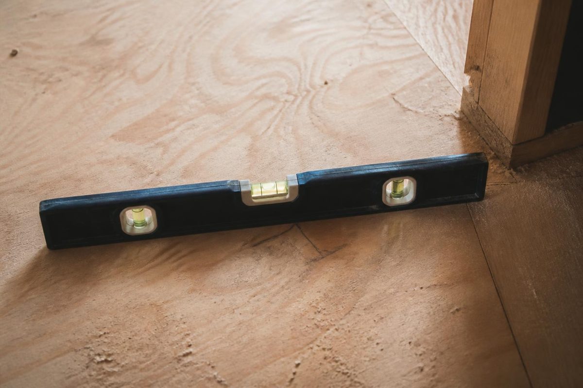 Worker checking a plywood subfloor for level before hardwood installation
