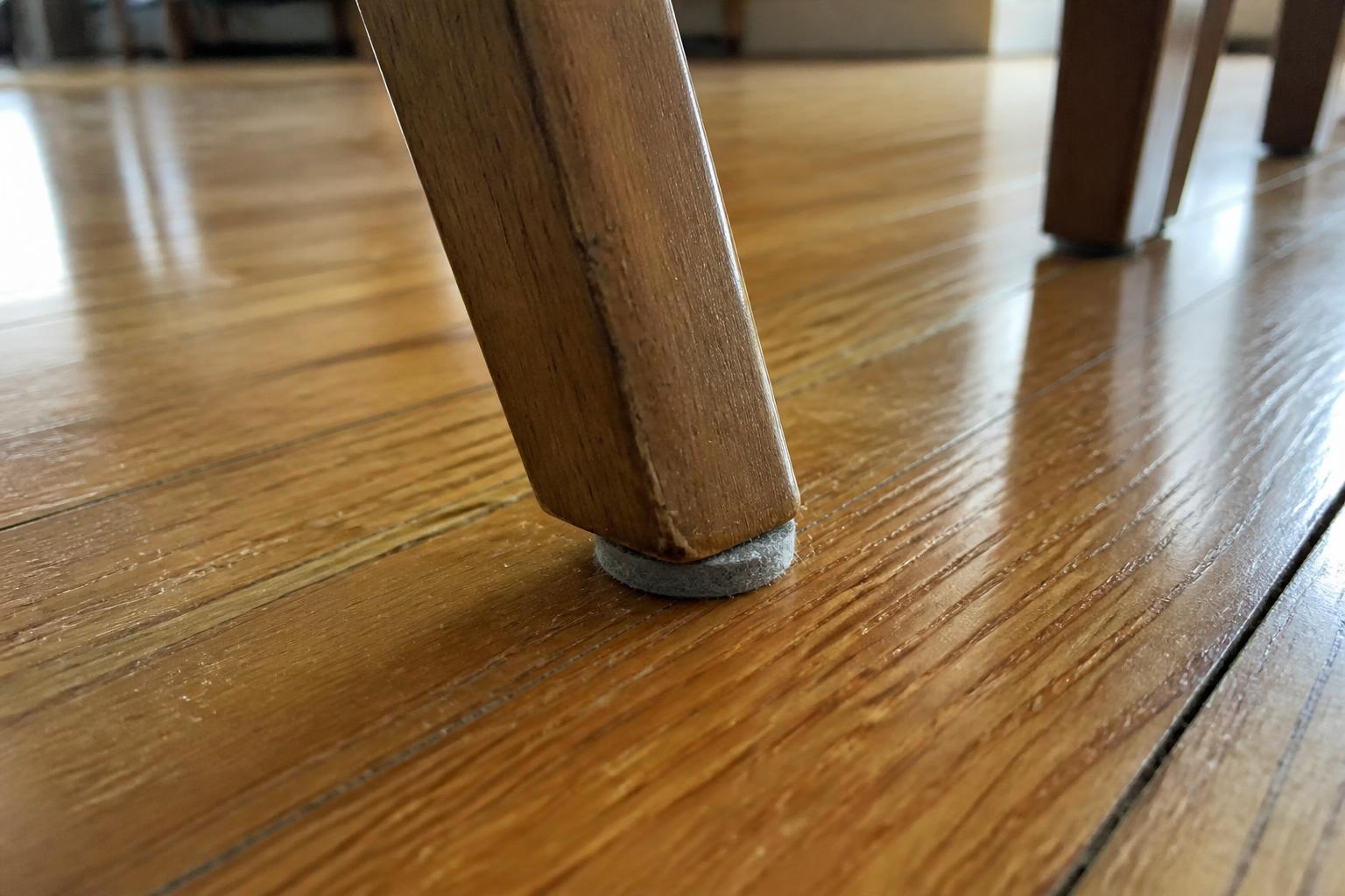 Felt furniture pads on the legs of a wooden chair on a hardwood floor